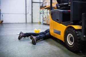 A worker is run over by a yellow forklift. Only their legs are visible.