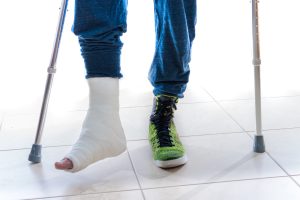 A person walks on crutches with a white case on one foot and a green trainer on the other