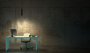 An office chair and desk under a lone light bulb in a dark room.
