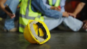 A hard hat on the ground, with someone holding their knee in pain in the background.