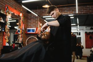 A barber trims a man's bread which could cause a hairdresser injury. 