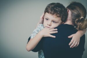 A small male child with a sad look on his face hugging an adult woman. 