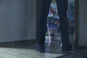 A man stood infront of a child's bedroom. A teddy bear is in the middle of the floor in the doorway. 