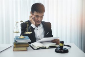 A solicitor researches multiple injury claims at a desk with books, scales and gavel. 
