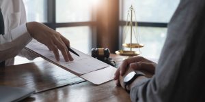 A man who stood on a nail at work discussing important documents with his solicitor. There is a gavel hammer and set of justice scales in the background