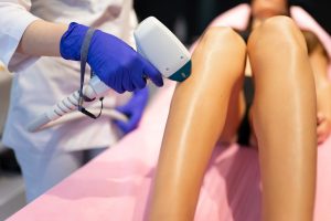 A woman uses a laser hair removal device on a client's leg