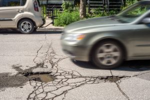 A large pothole in the road which a car is about to hit