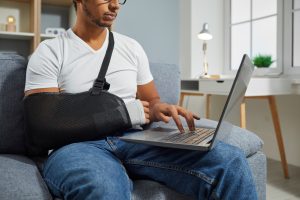A man with a broken arm researching personal injury claims on a laptop