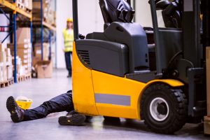 An injured worker lays in front of a forklift truck. 