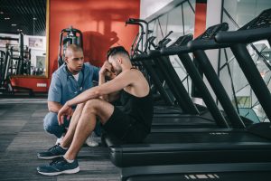 Man sitting with injuries sustained from using treadmill while someone assists him.