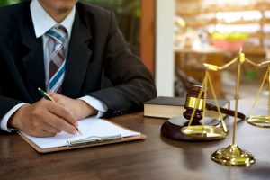 Solicitor holding pen working on a gym accident claim whilst sat at a desk by a set of gold scales and a wooden gavel.
