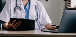 A doctor examining medical evidence on a laptop and clipboard