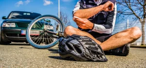 A cyclist sits in front of a car with their helmet on the ground after an accident