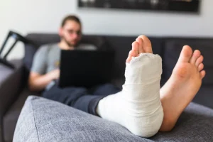 An injured man rests on a sofa, using a laptop to search for solicitors.