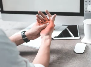 A person sitting at their desk holding their hand in pain which is highlighted by a red glow.