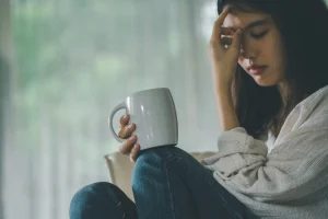 Woman drinking coffee in front of a window in a domestic abuse refuse. 