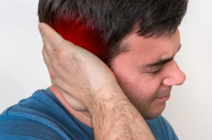 A man holding the back of his head in pain which is highlighted by a red glow.