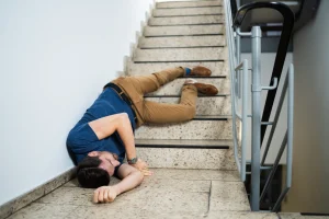 A man lays unconscious at the bottom of a staircase.