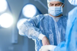 A close up of a male surgeon operating on a patient with white lights in the background.