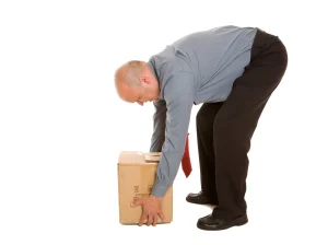 A man trying to lift a heavy cardboard box with the incorrect lifting technique.