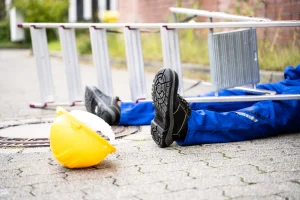 A worker's legs trapped under a ladder with a hardhat to the side after a fall from height. 