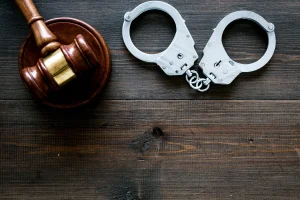 A gavel and a pair of handcuffs on a wooden table.