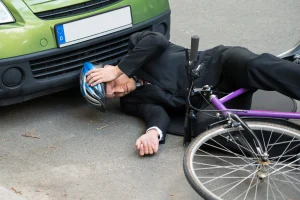 A rider on the ground holds his helmet after being left with physical injuries because of someone else's negligence.