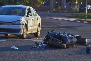 A damaged car and debris on road after a motorcycle accident caused multiple severe injuries.